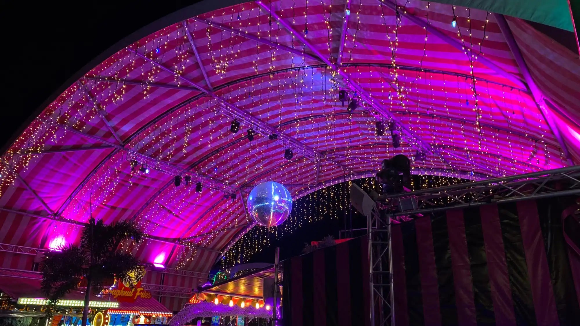 Curved archway illuminated with pink lights and hanging crystal-like decorations beneath a disco ball.