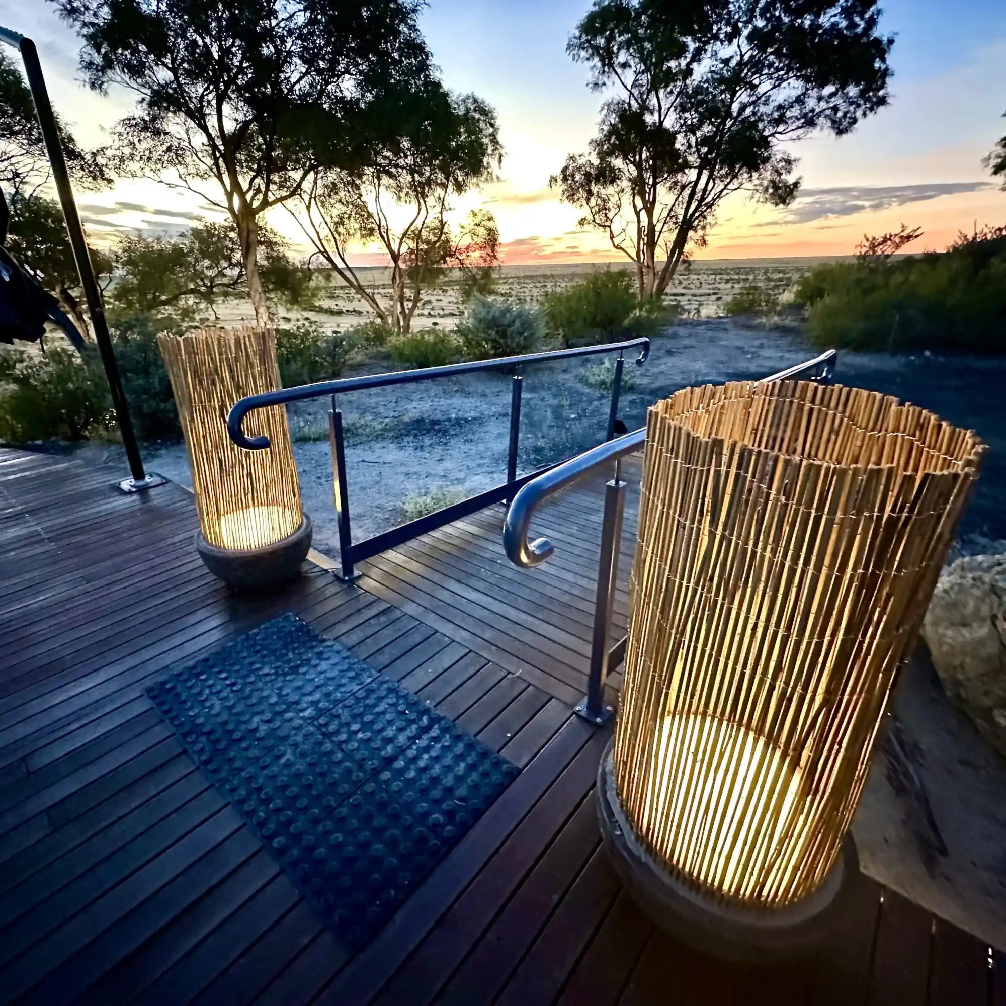 Illuminated bamboo lanterns on a wooden deck with glass railing.