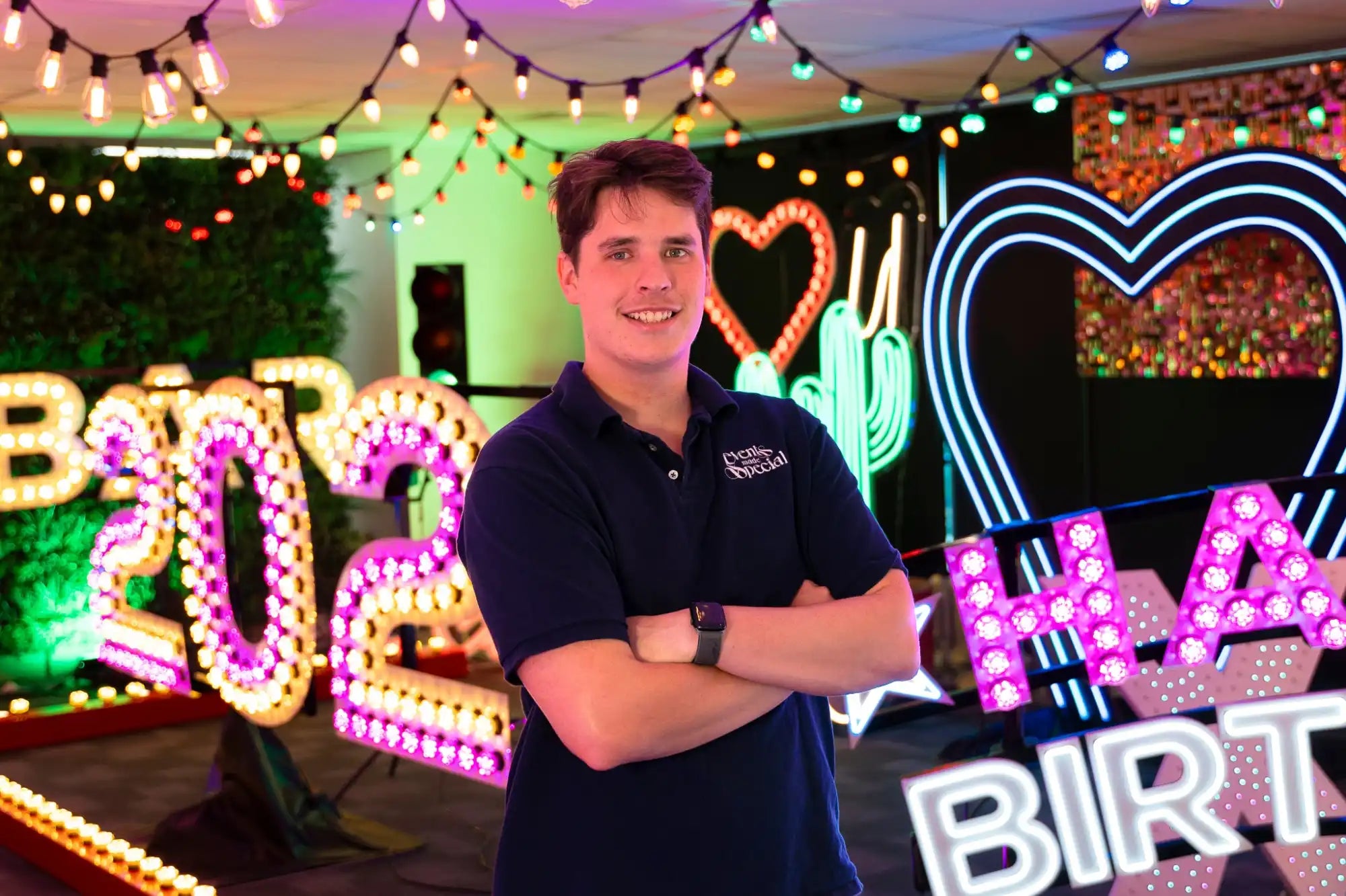 A person wearing a navy blue polo shirt stands with arms crossed.